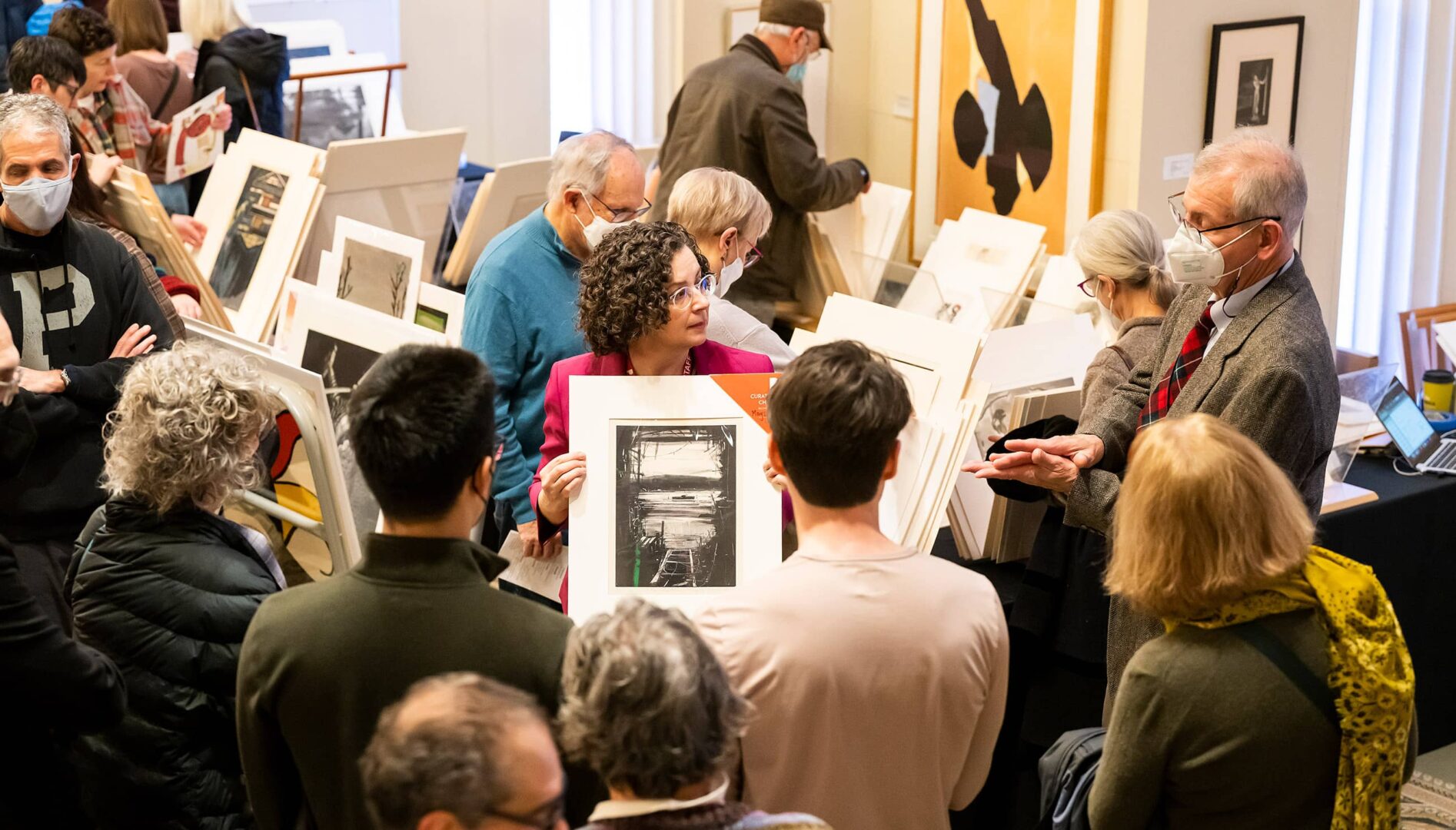 A group of people gathered around an individual holding up a print.