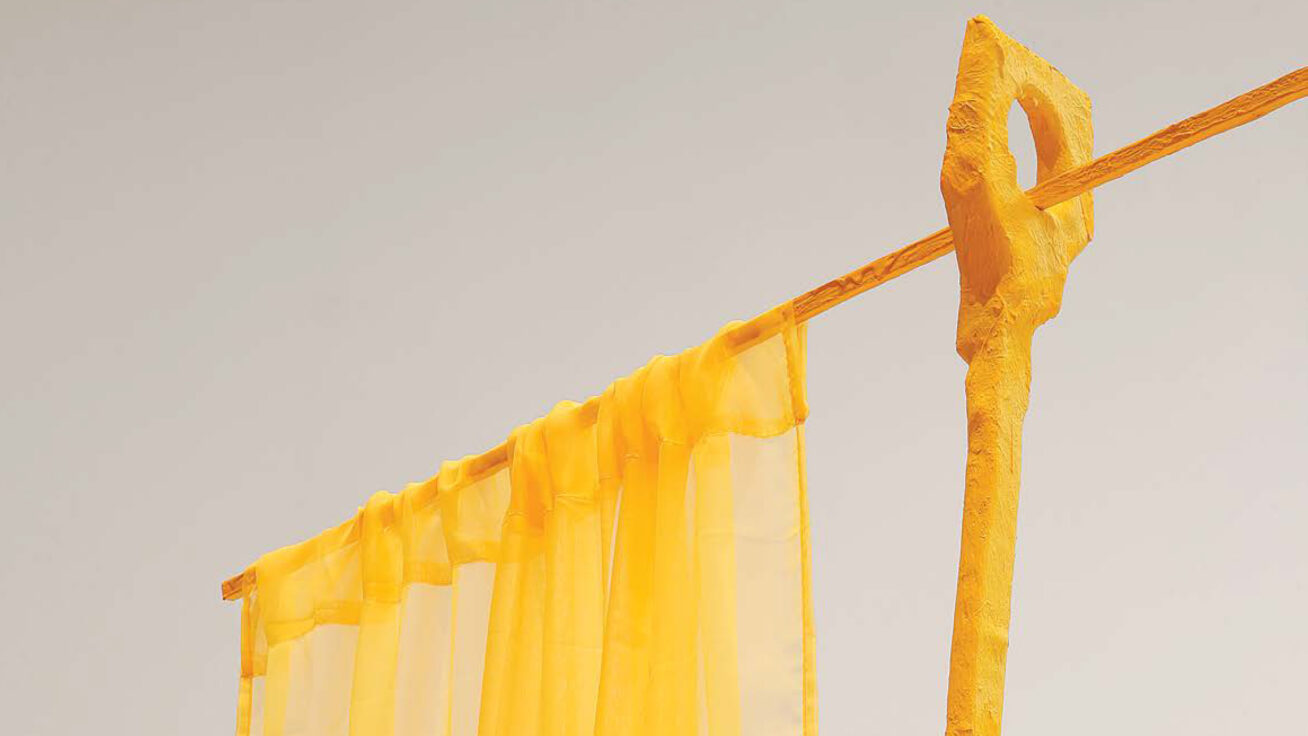 Detail of a yellow sculpture with a curtain-like rod and hanging fabric