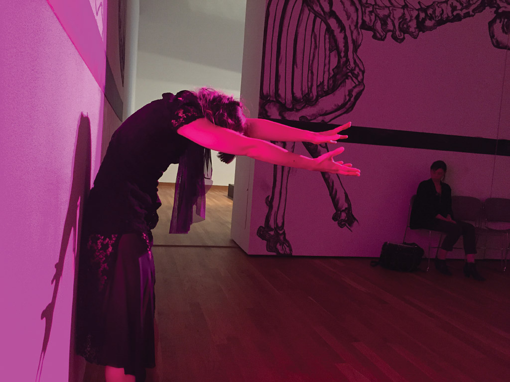 Photograph of a woman dancing against a wall washed in pink light