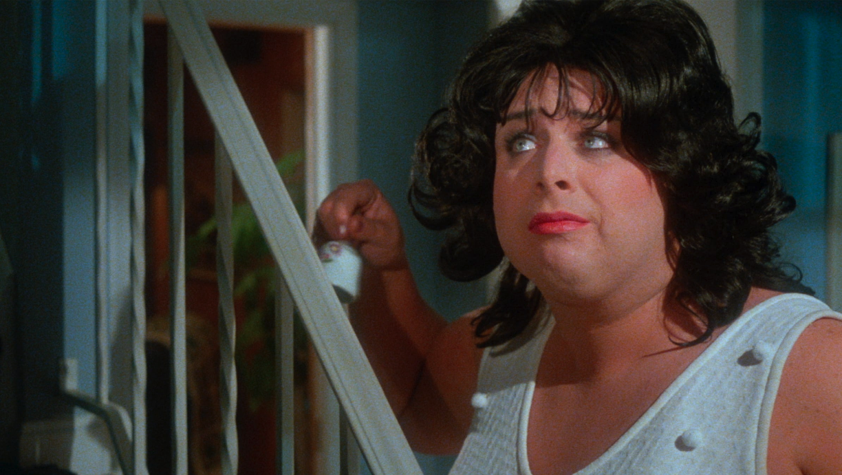 Film still from John Waters movie Polyester, of Divine standing at the bottom of a staircase