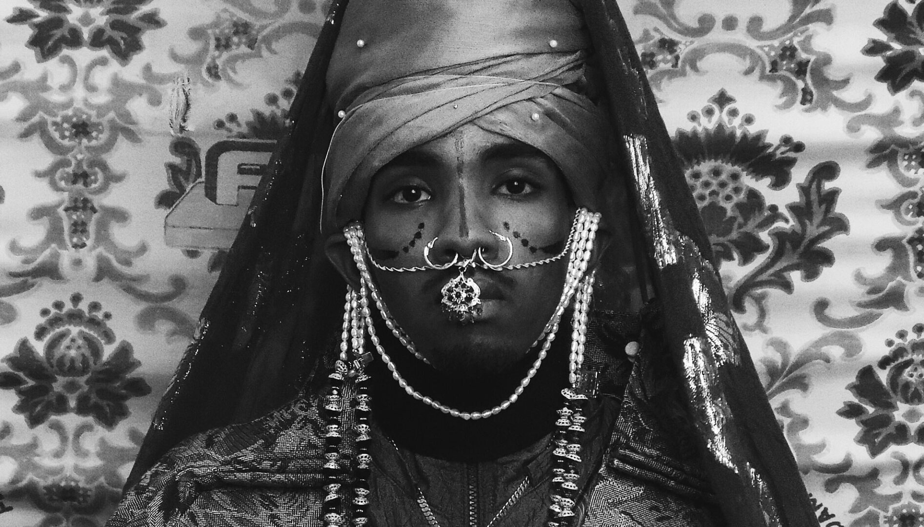 Black and white photograph of a person wearing heavy jewelry and a large head wrap