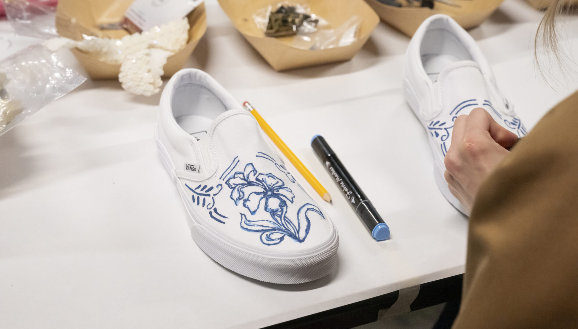 Photo of a white sneaker with blue writing on it, surrounded by craft supplies