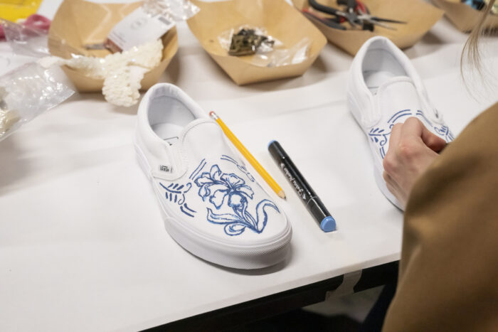 Photo of a white sneaker with blue writing on it, surrounded by craft supplies