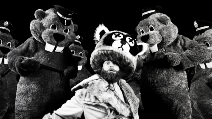 Black and white photo of a man in a costume with people in beaver costumes surrounding him