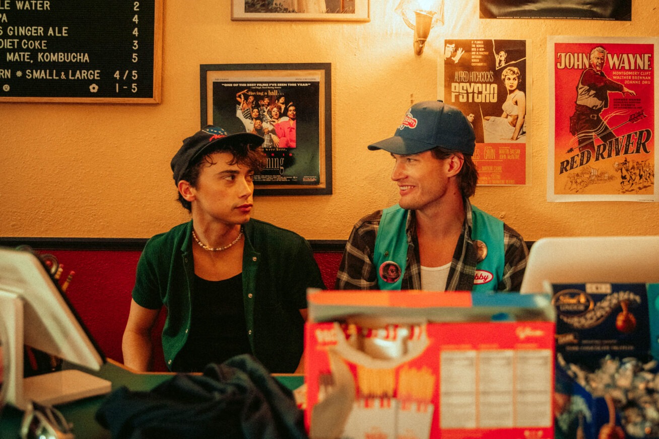 Photo of two people looking at each other in baseball hats sitting behind the counter of a movie theater