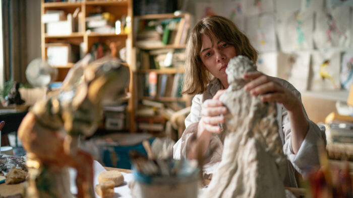 Film still of a woman working on a clay sculpture