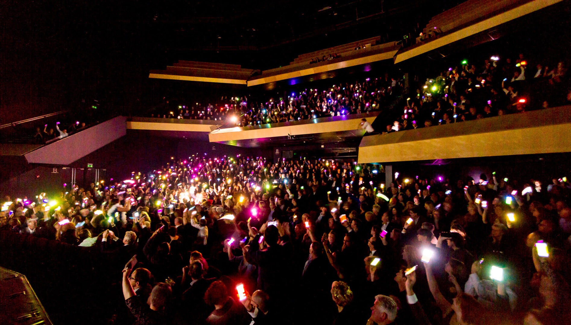 A dark auditorium with hundreds of people holding up their illuminated cellphones