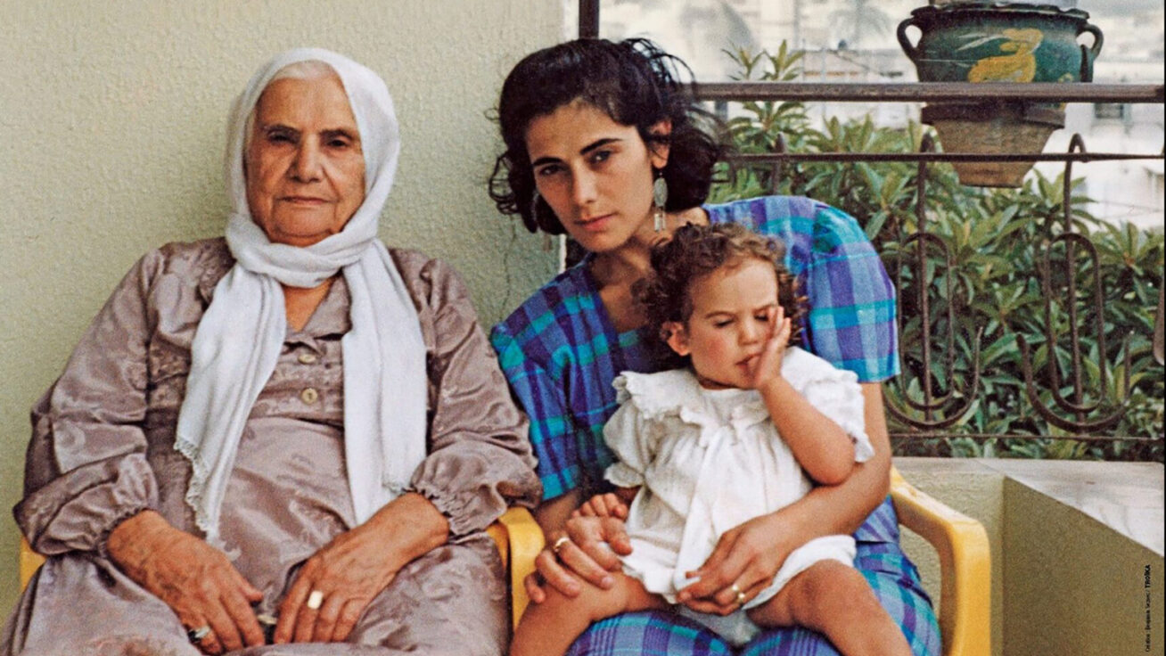 Photo of three people: an older woman with a white headscarf, a young mother in a blue dress, and a young girl in a white jumper
