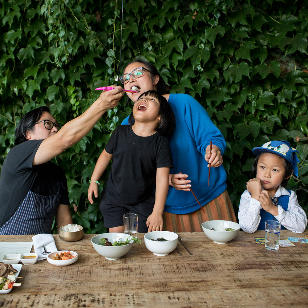 Peter Cho and Sun Young Park with two children sharing food at an outdoor table.