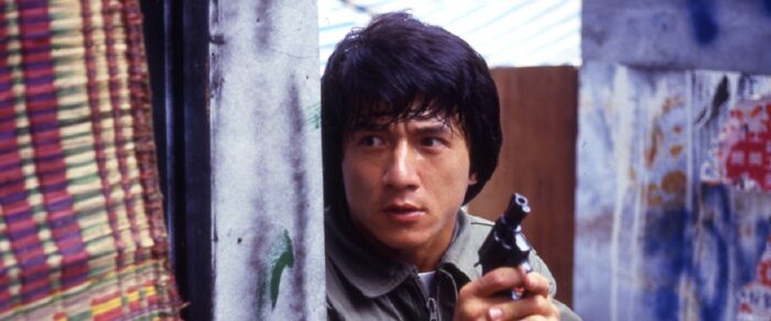 Photo of Jackie Chan hiding in a doorway holding up a gun