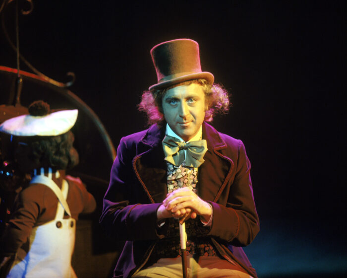 Photo of Gene Wilder in his costume for Willy Wonka, a purple velvet coat, tophat, and a cane