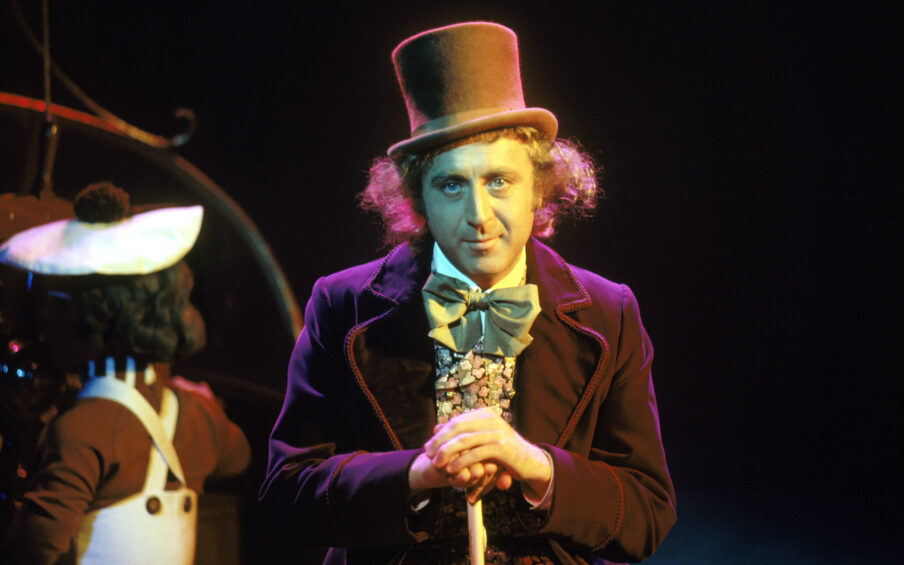 Photo of Gene Wilder in his costume for Willy Wonka, a purple velvet coat, tophat, and a cane