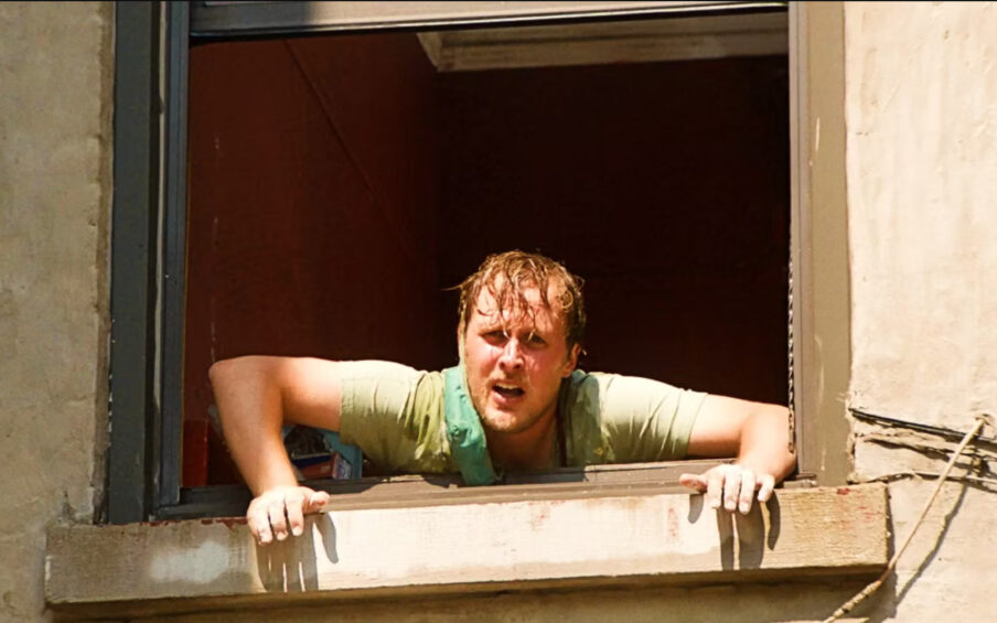 A man with red short hair hanging out a window