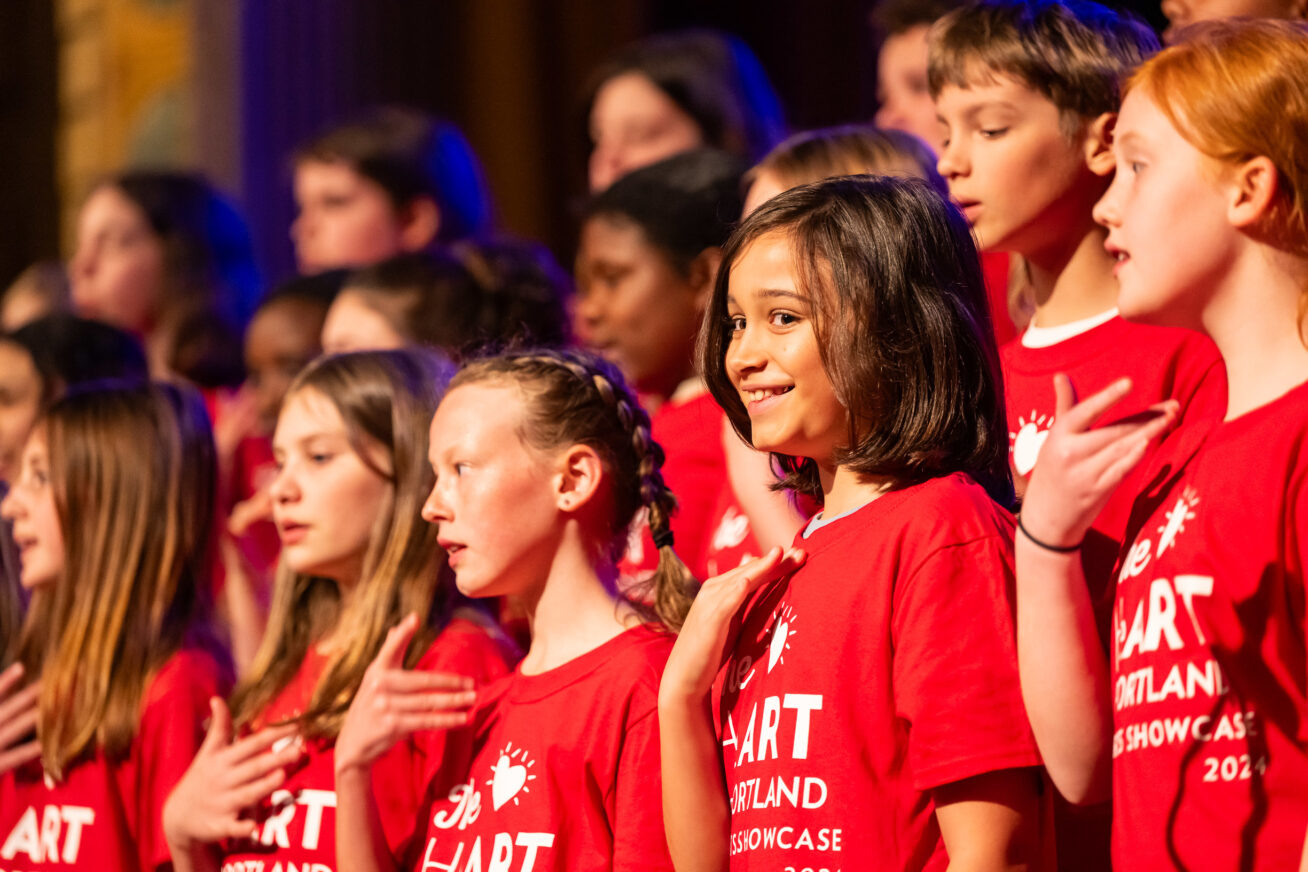 Photo of a group of kids in red HeART of Portland t-shirts on stage