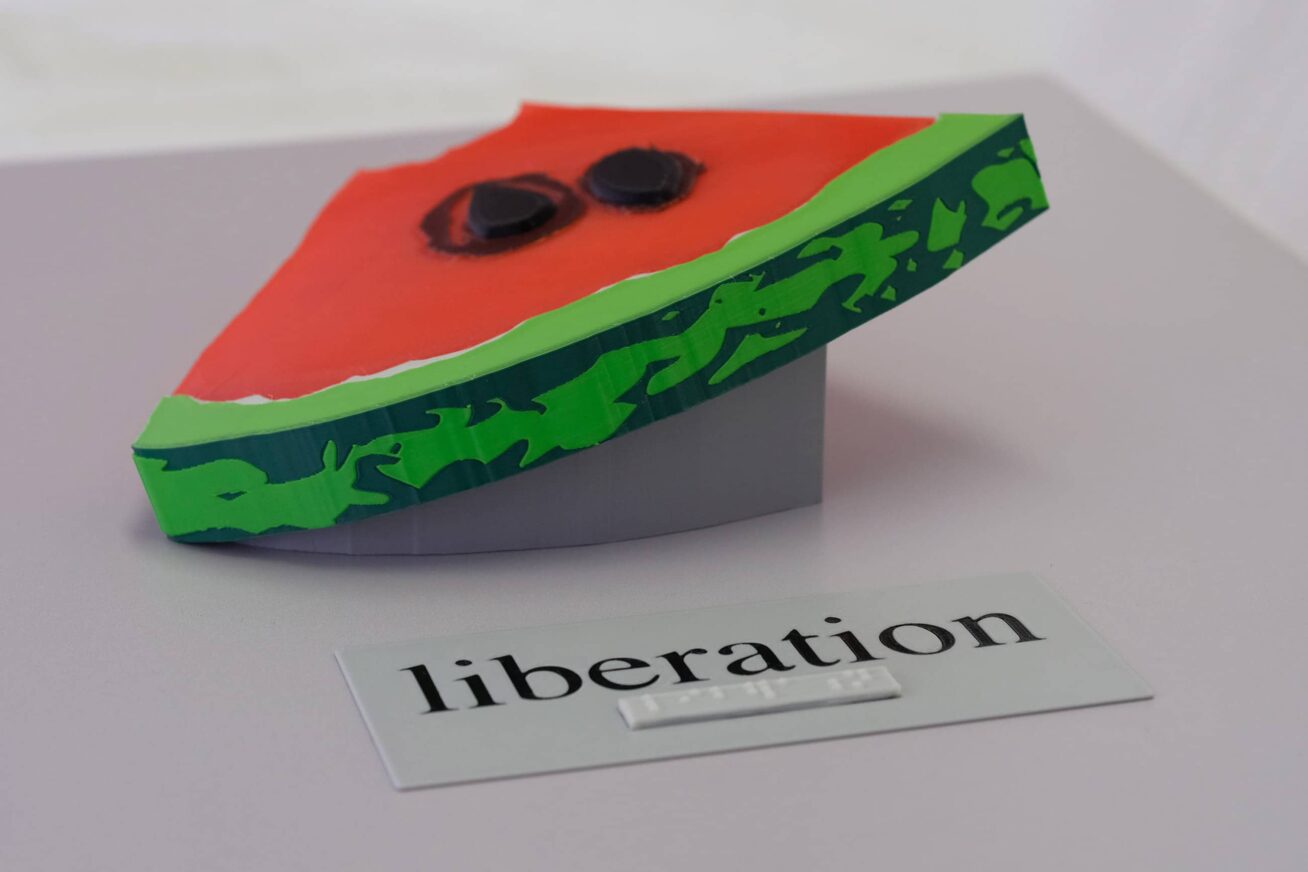 3-D printed replica of a slice of watermelon mounted on a panel with the word "liberation" printed as text and in braille.