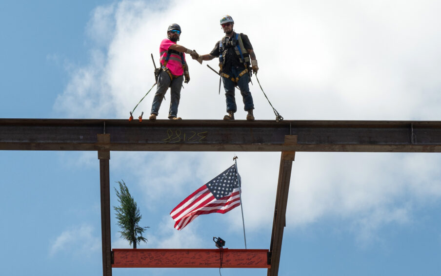 Two construction workers on top of a steel beam shaking hands