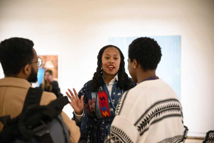 Photo of a Black woman in a gallery talking to two visitors