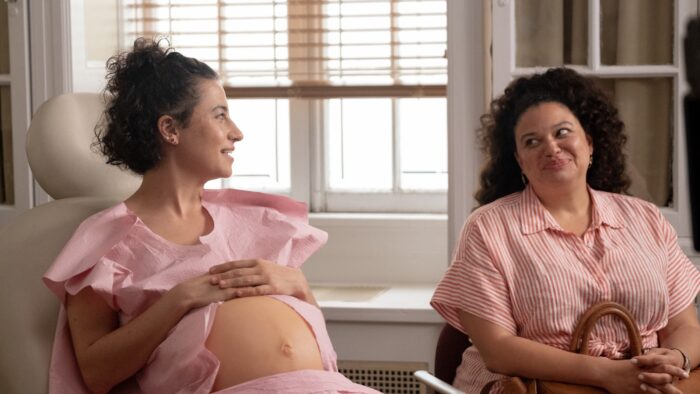 Photo of a pregnant woman in a doctor's chair smiling and talking to her friend seated next to her.