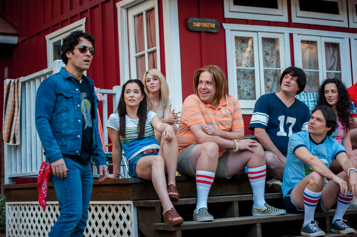 Film still with a group of camp counselors sitting outside a red cabin.