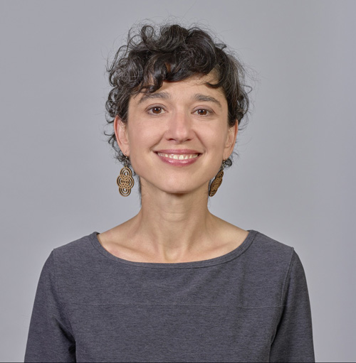 Portrait of a woman with curly brown hair and a grey shirt, smiling