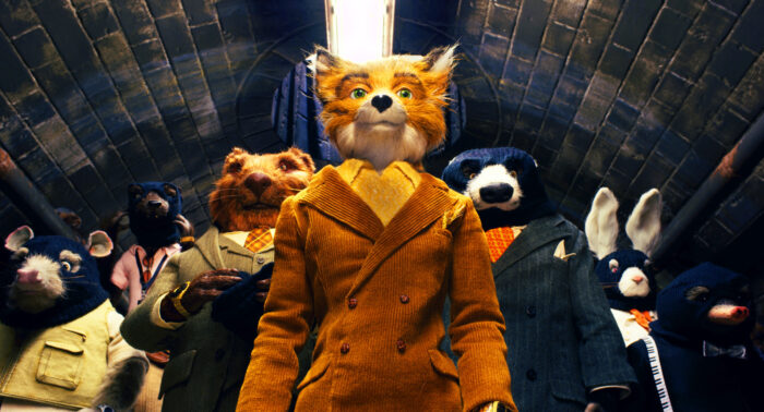 Animated film still of a fox in an orange corduroy suit standing in front of a group of other animals