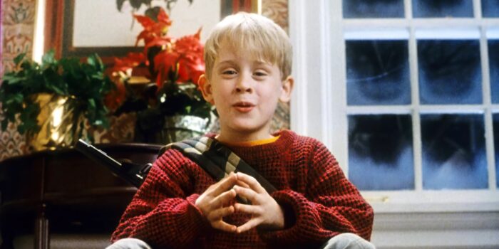 A young blond boy with a red sweater sitting with a frosty window and Christmas decorations behind him