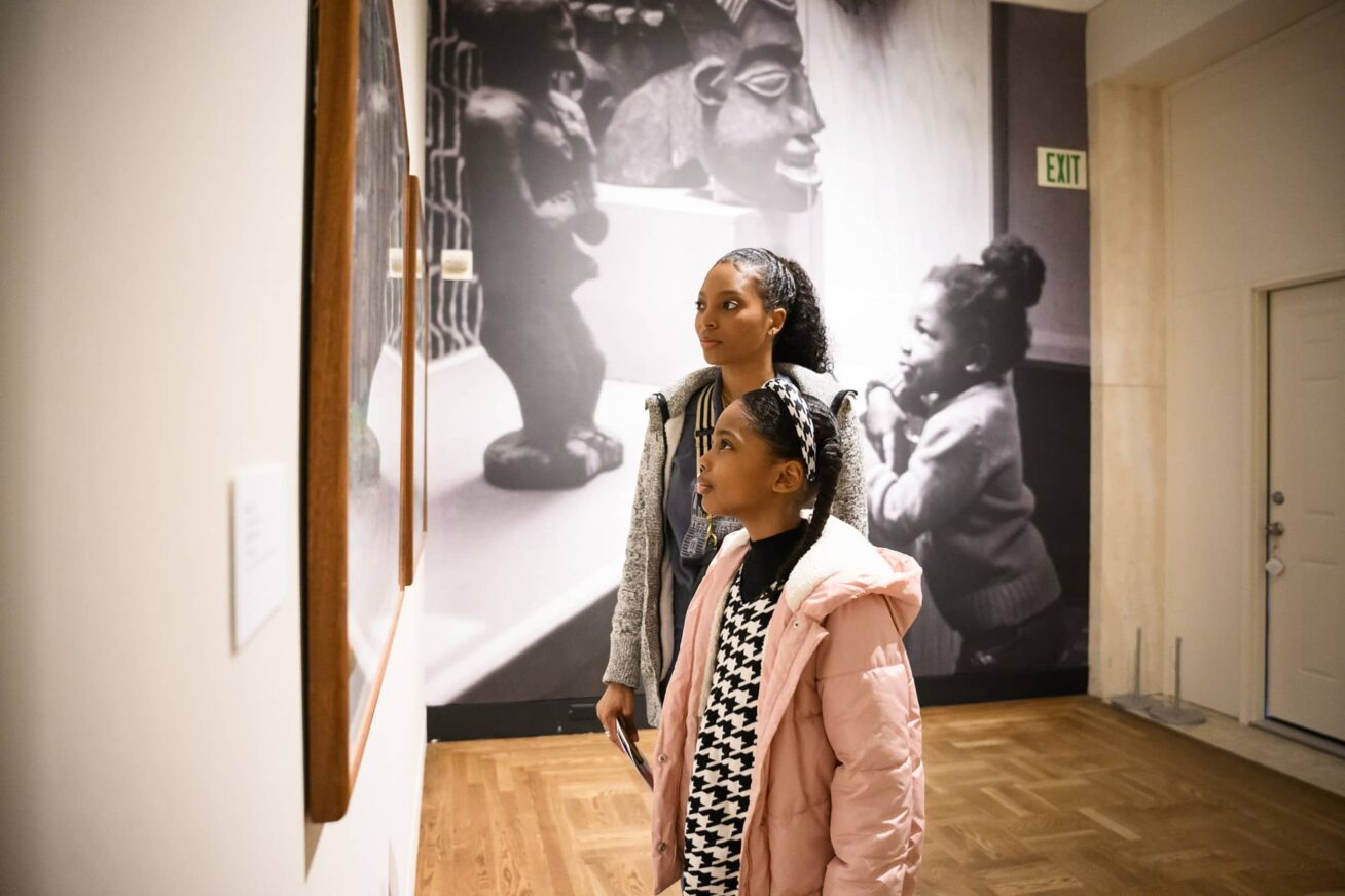 Two people looking at artwork hanging on a wall.