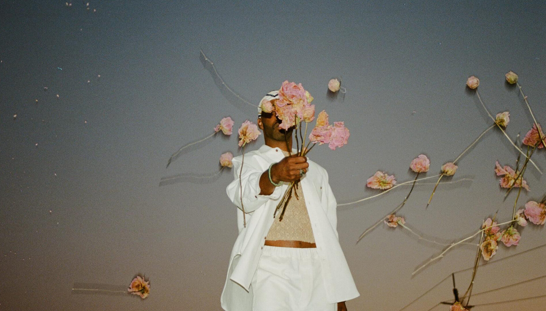 Photo of a Black person in a white outfit holding and throwing pink flowers