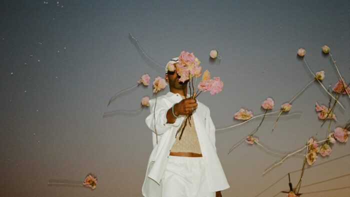 Photo of a Black person in a white outfit holding and throwing pink flowers