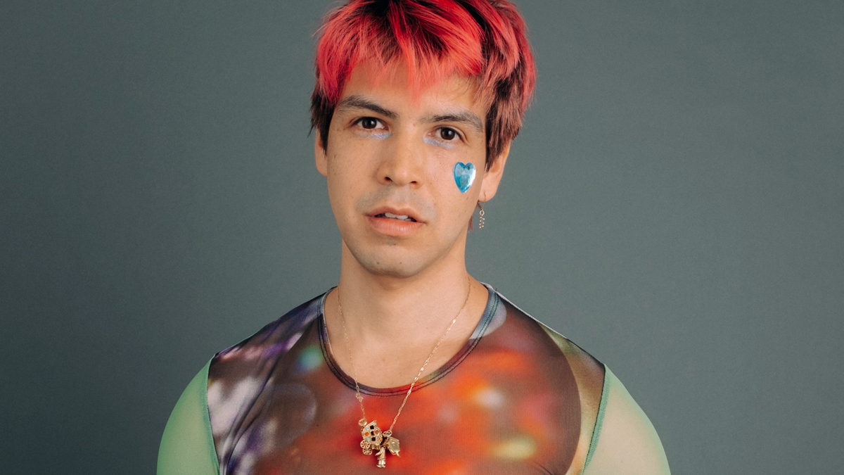 Photo of a young man with bright red hair and silver sparkly makeup and a heart on his cheek