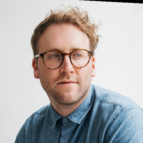 Portrait of a white man with blonde curly hair and tortoise shell glasses