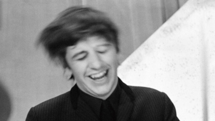 Black and white photo of Ringo Starr with his eyes closed and laughing, swinging his hair to the side