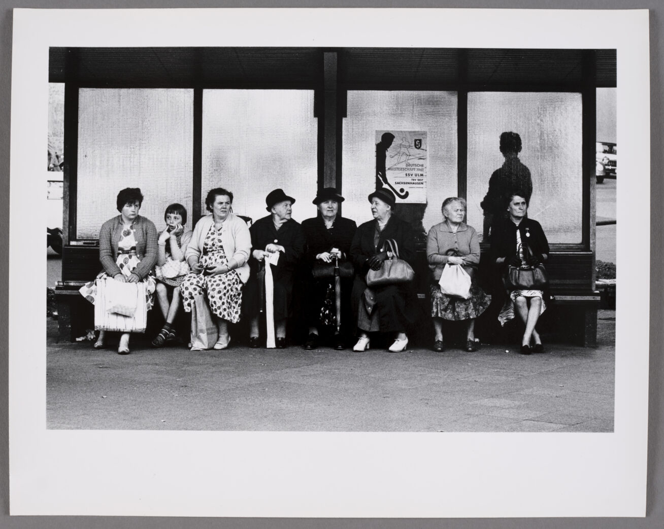 Black and white photograph of a group of women and a young girl sitting at a bus stop