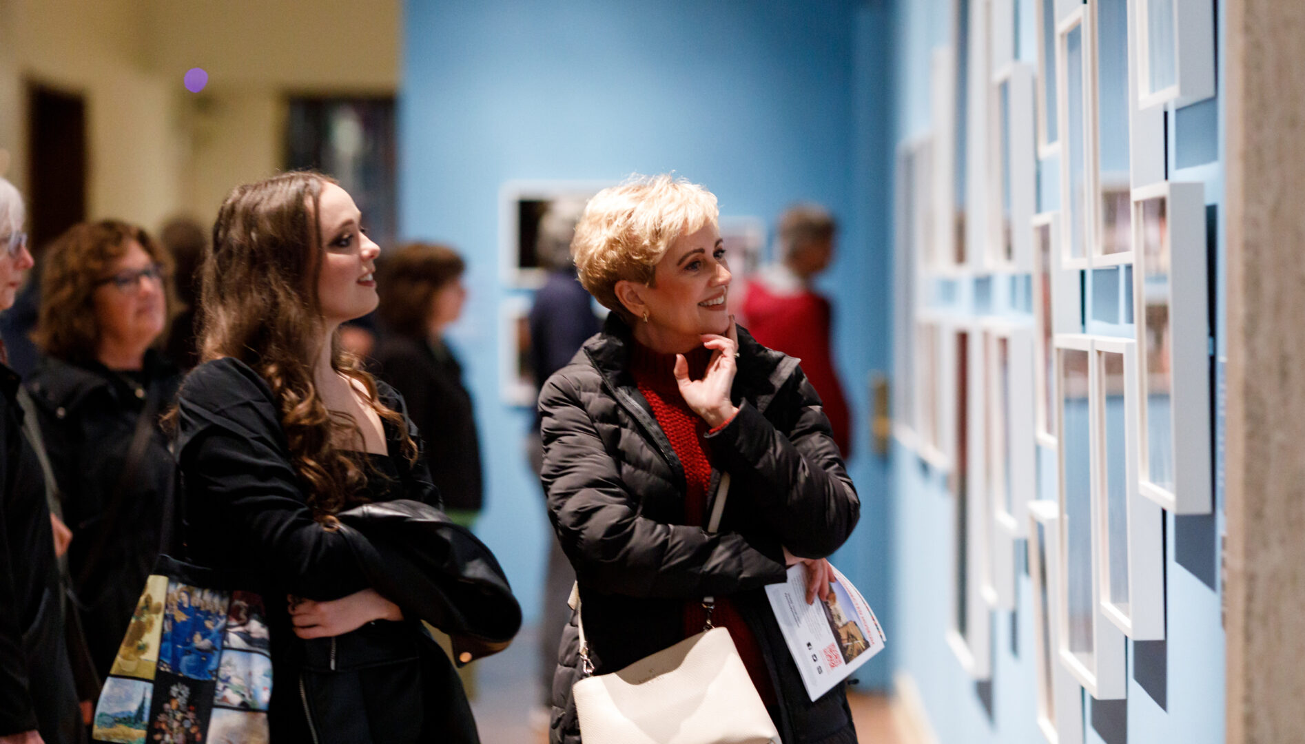 A smiling woman looking at photographs hanging in white frames on a light blue wall