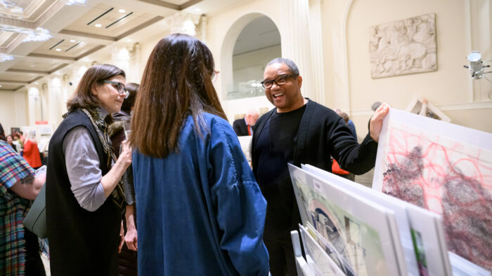 A small group of people looking at prints and conversing.