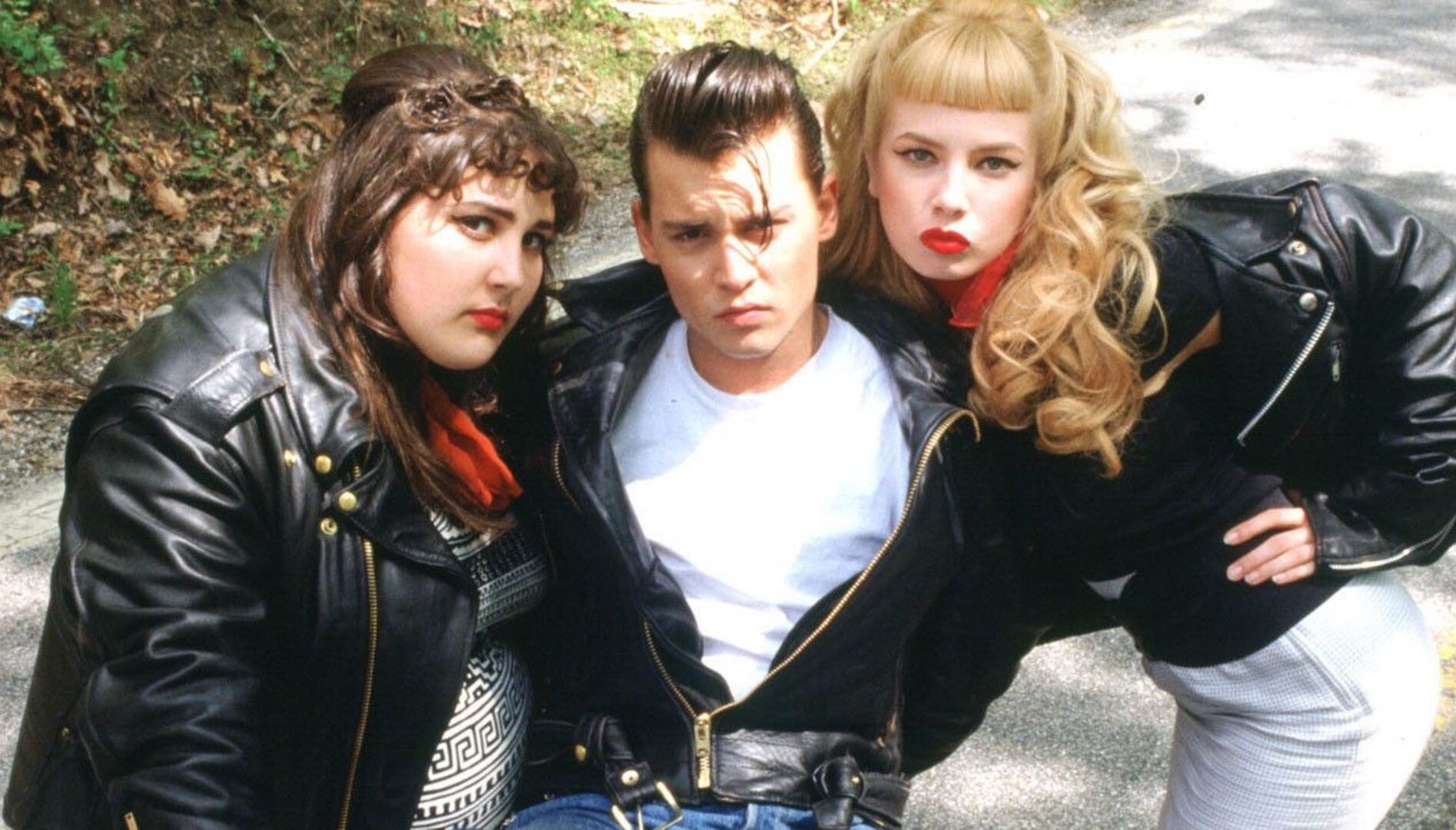 Two young women and one young man in the middle, all wearing black leather jackets and 1950s-looking haircuts