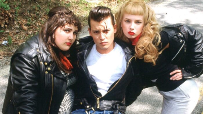 Two young women and one young man in the middle, all wearing black leather jackets and 1950s-looking haircuts