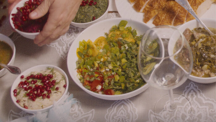 Photo of a table with multiple bowls of food on it and a hand reaching to the food from the upper left corner