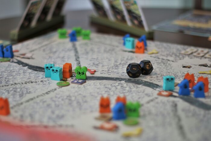 A close up photo of a game board with colorful animal-shaped game pieces and black dice