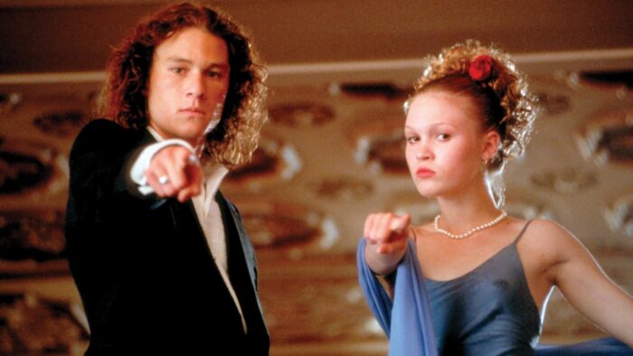 A teenage boy and girl, wearing formal clothes, point down toward the camera.