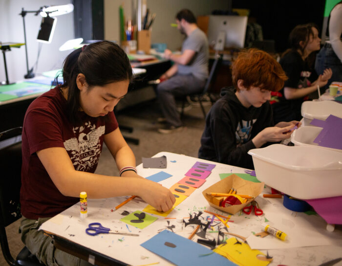 Photo of a young woman sitting at a table and concentrating on art that she's making