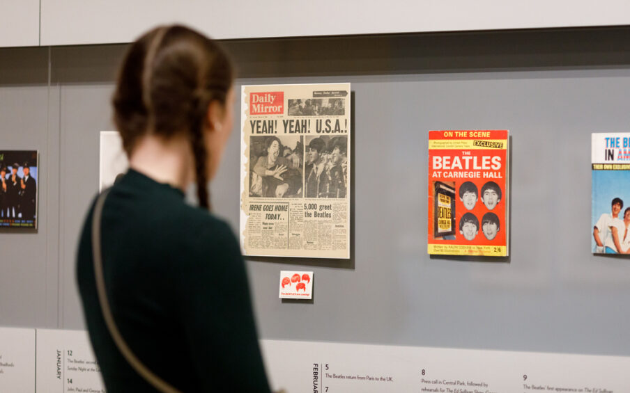 A visitor is looking at a case of Beatles ephemera, newspapers, and magazines in a gallery.