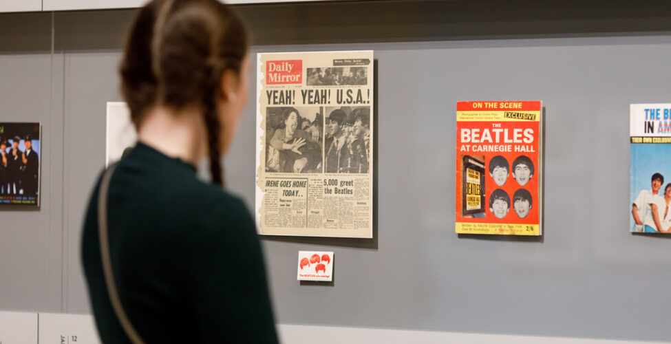 A visitor is looking at a case of Beatles ephemera, newspapers, and magazines in a gallery.