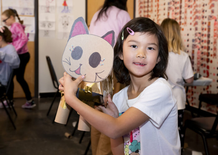 A photo of a girl holding up a cat mask made of cardboard