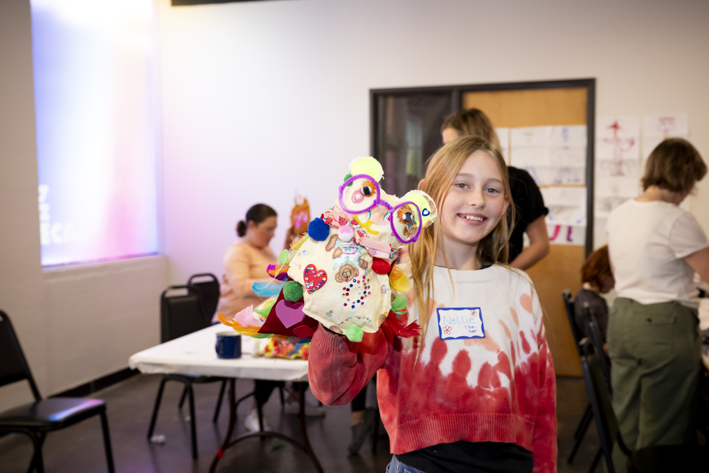 Photo of a girl with long blond hair and a red and white sweater holding up a creature she crafted