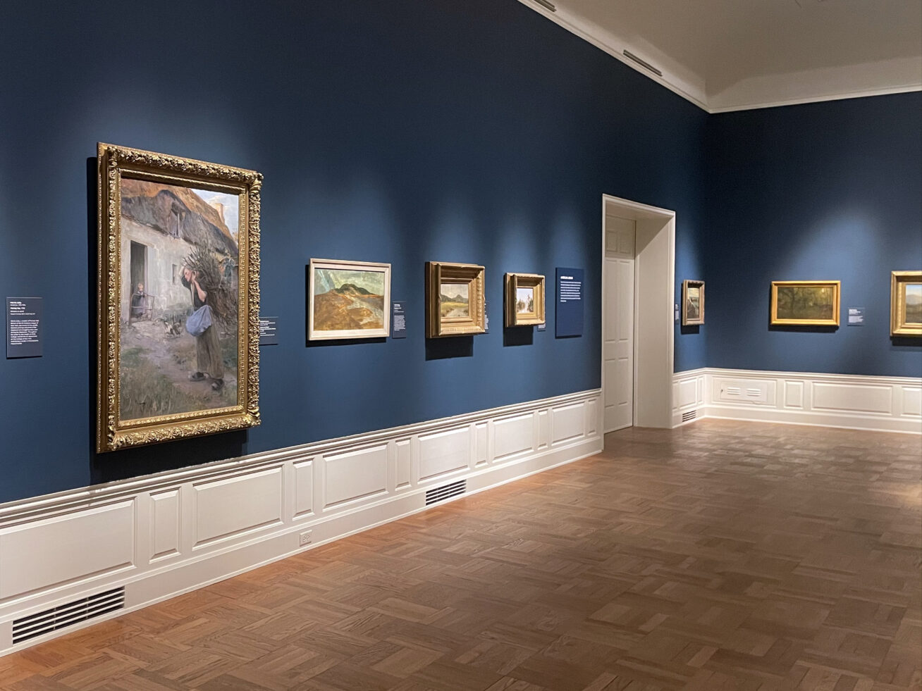 Artworks hanging in a gallery with dark blue walls.