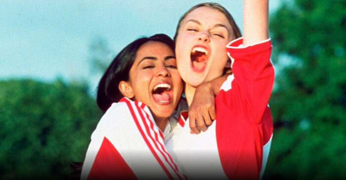 Two teenage girls in red and white soccer uniforms hugging and cheering