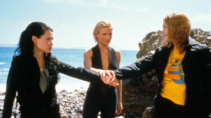 Three women standing in front of the ocean. Each one is holding a hand into the middle between them.