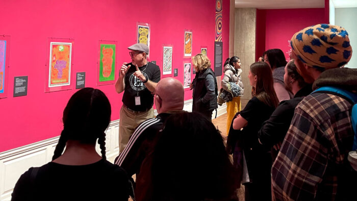 Tour attendees of varying age, gender, and ethnicity stand across from a presenter.