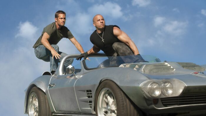 Two men stand on the top of a silver sports car